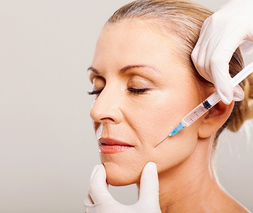 Gloved hands injecting BOTOX® into older woman’s cheek