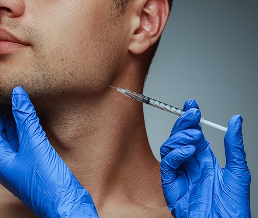 Blue gloved hands injecting BOTOX into man’s jawline