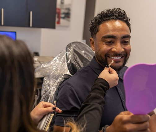 Cosmetic dentist holding a veneer in front of a patient's tooth