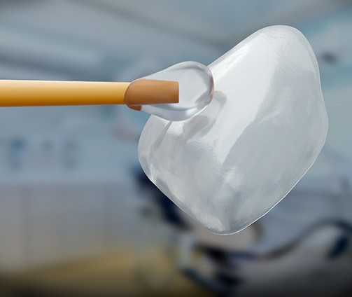 Woman in dental chair gesturing to shade guide being held to her smile