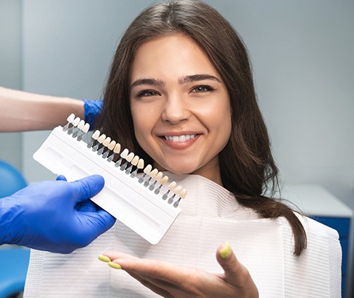 Man in dental chair smiling at his reflection in handheld mirror with dentist in the background