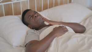 Man lying in bed holding face in pain from toothache.