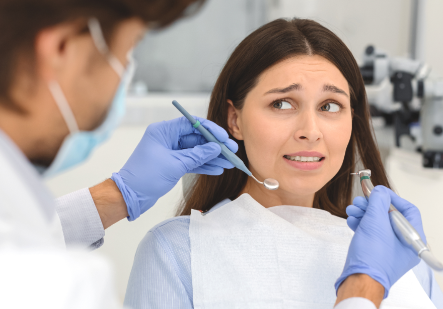 Woman looking nervous in dental chair while dentist holds tools over her